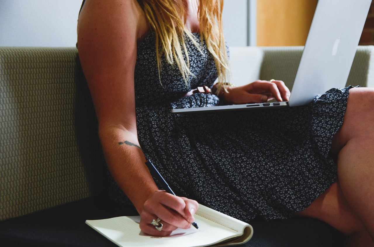 woman writing in notebook with laptop open